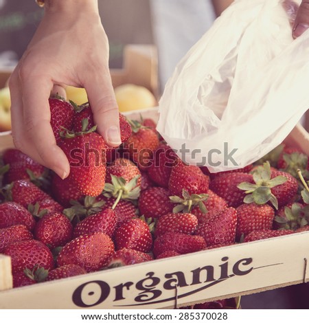 Red fresh tasty strawberries on a wooden box being picked up by a white girl hand on a fruit market.