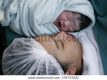 Baby Just Born in Mother Embrace.Delivery room in hospital. Baby drape in white cloth show only face.