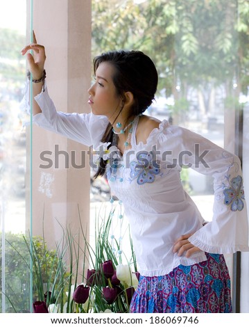 Girl in trendy fashion action. Her hand lean against glass window look forward to someone.window lighting shot.
