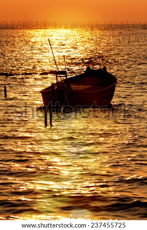 Fisherman boat float on the sea at sunset.Ripple and sky are orange of warm tone.Boat in shadow.