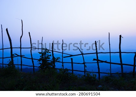 Dark tree and fence stick in shadow at foreground.Mountain at background.Sun nearly go down.