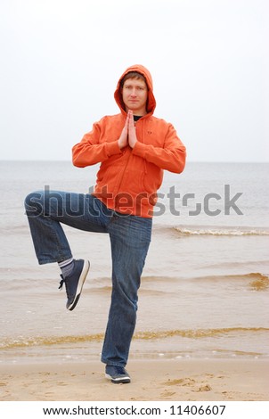 Young man in casual clother doing yoga on the seaside