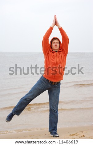 Young man in casual clother doing yoga on the seaside