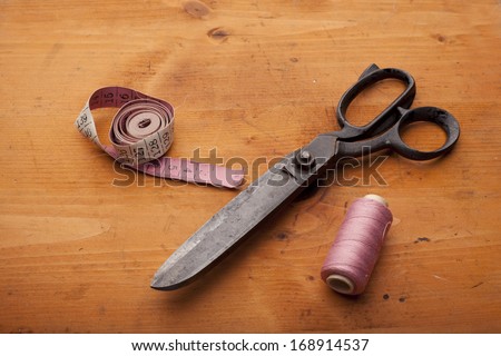 dressmaker shears craft concept with spool and measuring tape on wooden texture