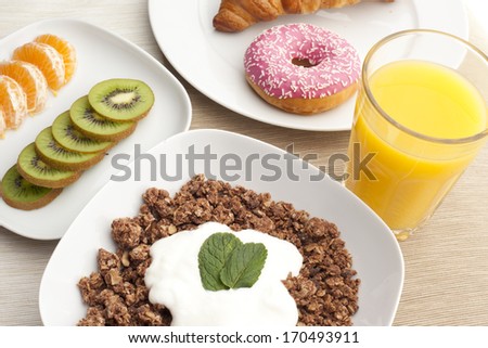 A healthy breakfast with croissants, muesli, yogurt, mint, juice, kiwi and mandarin on white plates