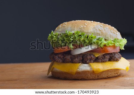 Delicious cheeseburger stacked high with a juicy beef patty, cheese, fresh lettuce, onion and tomato on a fresh bun with sesame seed standing on dark blue on a wooden tabletop with copyspace