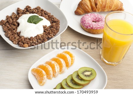 A healthy breakfast with croissants, muesli, yogurt, mint, juice, kiwi and mandarin on white plates
