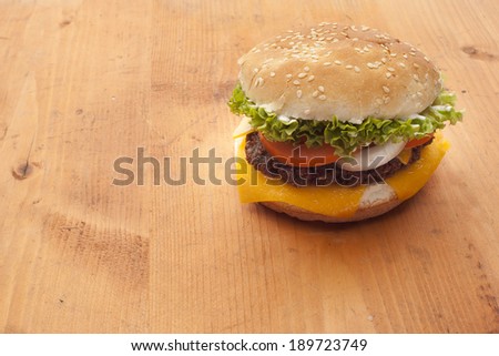 Delicious cheeseburger stacked high with a juicy beef patty, cheese, fresh lettuce, onion and tomato on a fresh bun with sesame seed standing on dark blue on a wooden tabletop with copyspace