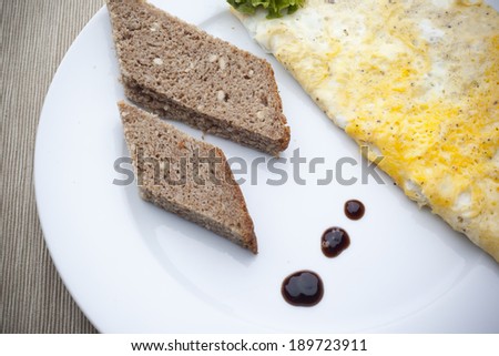 Egg omelette with balsamic vinegar and sunflower bread slices with a dash of balsamic vinegar on a porcelain plate