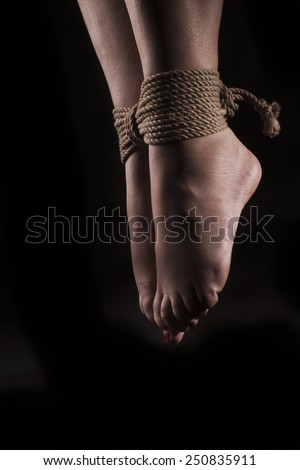 detail suspended bound feet submissive young girl on a black background / BDSM theme