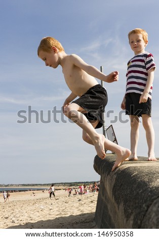 Six year old boy jumping from promenade onto beach. While twin brother watches on.
