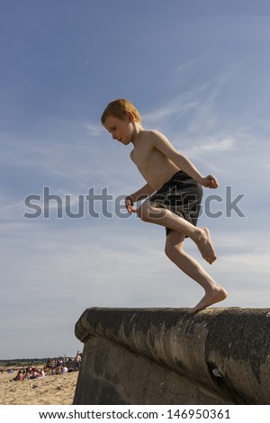 Six year old boy jumping from promenade onto beach.
