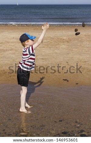 Six year old boy playing at throwing rocks into beach pool.