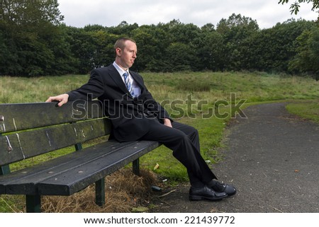 Young man, business man, dressed in suit. Sitting on a park bench.