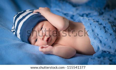 Newborn baby boy with blue beanie lies awake under blue blankets