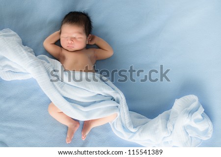 Newborn 4 day old baby boy lying on his back relaxing under a blue wrap cloth