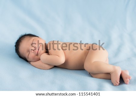 Newborn 4 day old baby boy lying on his side smiling to himself