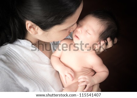 Young Asian mother lovingly holds her newborn baby boy (5 days old)