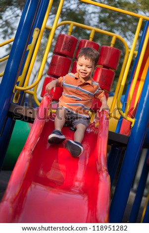 Happy 2 year old boy riding a red slide in an outdoor playground