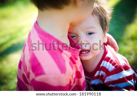 Older brother comforts his crying baby brother outdoor in the park
