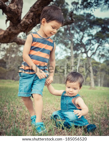 Two mixed race Asian Caucasian brothers. The older 4 year old brother teaching the younger 18 month old baby to take his first steps