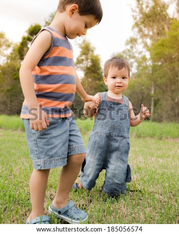Two mixed race Asian Caucasian brothers. The older 4 year old brother teaching the younger 18 month old baby to take his first steps