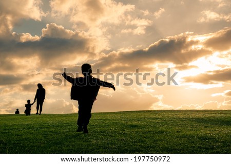 Family silhouette against a bright cloudy sky at sunset. Young boy running with family walking in background