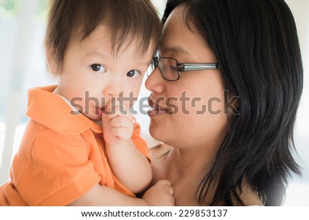 Cute mixed race 1 year old Asian Caucasian boy sucks his thumb and cuddles with his beautiful Asian mother.