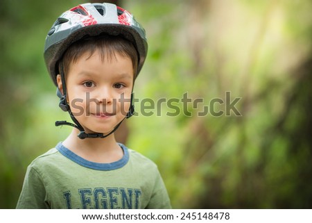 Cute 4 year old mixed race Asian Caucasian boy wears a bike helmet outside with a soft natural green background and copy space