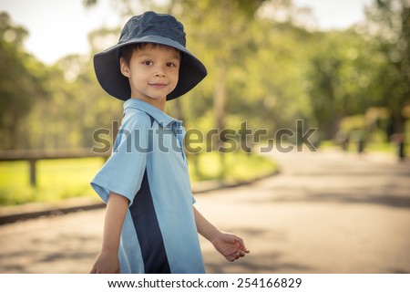 Mixed race Asian Caucasian boy confidently leaves home on his first day of school. Wearing uniform and sun hat. Walking down his suburban street in the summer sun