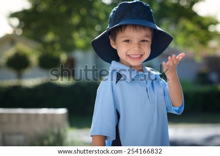 Mixed race Asian Caucasian boy confidently leaves home on his first day of school. Wearing uniform and sun hat. Turning to blow a kiss to his mom as he leaves his house.
