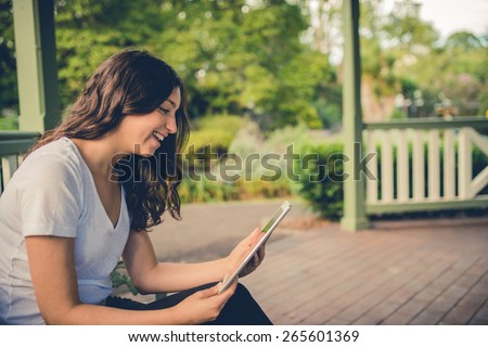 Pretty brunette girl video conferencing on her tablet computer outside in a park. Filtered effects