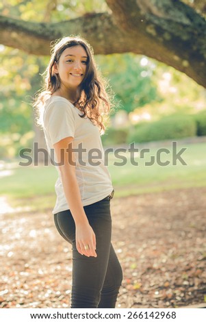 Pretty young caucasian woman wearing black jeans walking outside in a park and turning to look back. Filtered effects