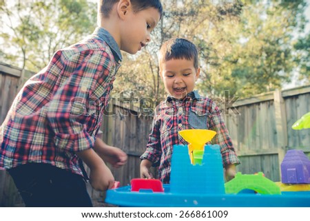 Cute 2 year old mixed race Asian Caucasian brothers play happily with a water toy in their suburban house backyard. Filtered effects