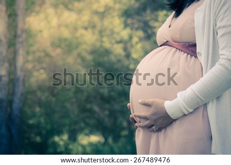 Beautiful Asian pregnant woman standing among trees, outdoor in nature. Filtered, vintage and soft focus effects