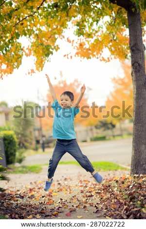 5 year old mixed race Asian Caucasian boy does a star jump (jumping jack) on the footpath (sidewalk) of his suburban neighborhood in Autumn (Fall)