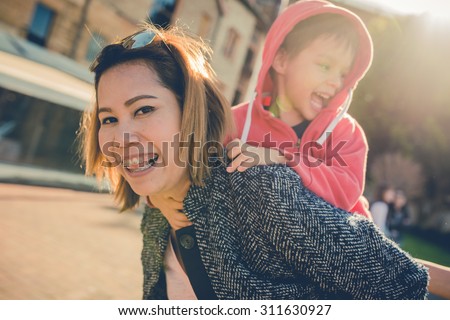 Asian Thai aunt plays with her 5 year old mixed race Asian Caucasian Australian nephew in the city. Filtered color shift, and sun flare effects.