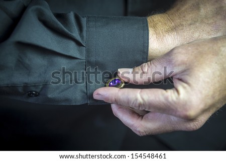 Cuff Link/ a close up of a man getting dressed in formal attire with a jewelled cuff link on a black shirt\'s sleeve