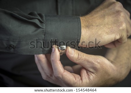 Cuff Link/ a close up of a man getting dressed in formal attire with a jewelled cuff link on a black shirt\'s sleeve