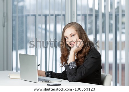 Portrait of a pretty business woman at office desk writing on document while talking on telephone.