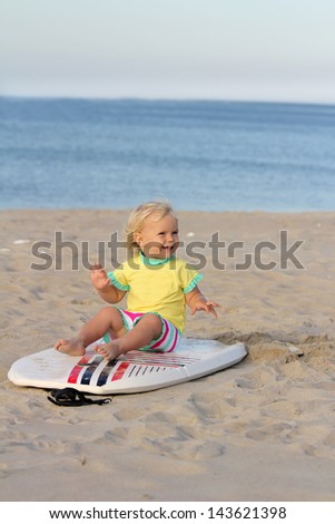 Happy toddler girl sitting on the boogie board on the beach