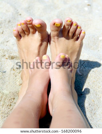 Two pair of feet with manicure: mother and little daughter on the beach sand