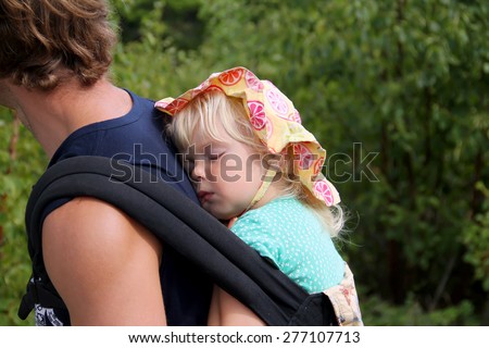 Sweet little girl slipping in the carrier on her father\'s back. Active family conception
