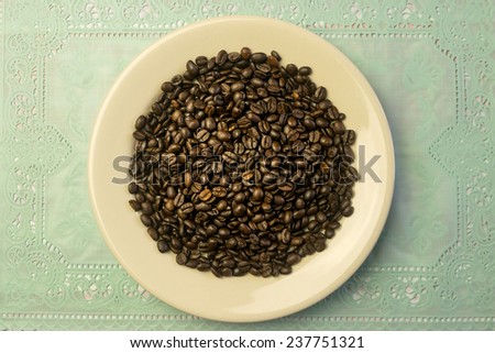 White round plate with a heap of coffee beans on a placemat