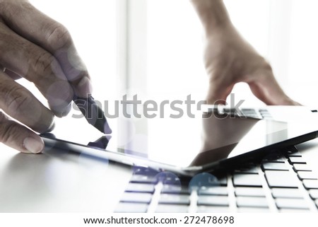 designer hand working with stylus and digital tablet and laptop on wooden desk in office