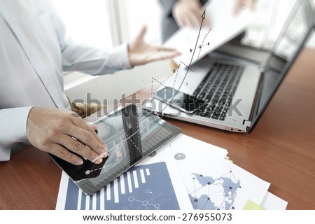business documents on office table with smart phone and digital tablet and laptop computer and two colleagues discussing data  and graph business diagram  in the background