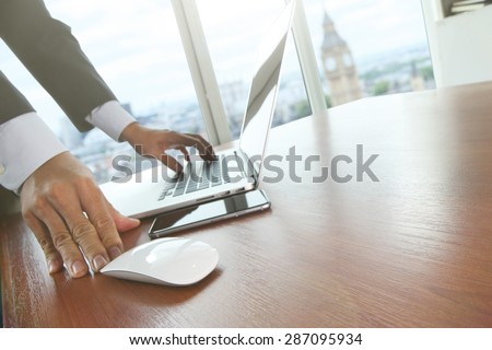 Close up of male hands on mouse and over black keyboard of laptop during typing with lon?on city blurred background