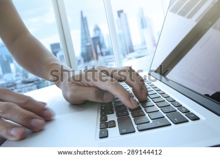 business man hand working on laptop computer on wooden desk with london city blurred background as concept