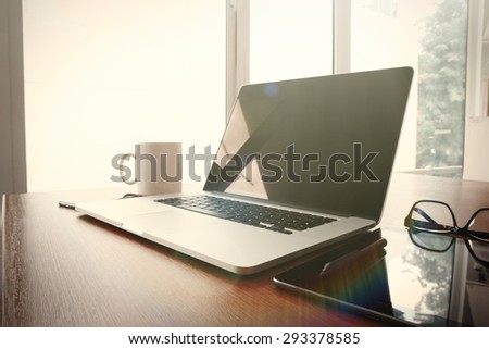 Office workplace with laptop and smart phone on wood table with eyeglasses on digital tablet