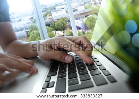 designer hand working with laptop computer with green plant foreground on wooden desk in office